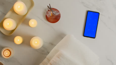 Overhead-View-Looking-Down-On-Still-Life-Of-Blue-Screen-Mobile-Phone-With-Lit-Candles-And-Incense-Stick-As-Part-Of-Relaxing-Spa-Day-Decor